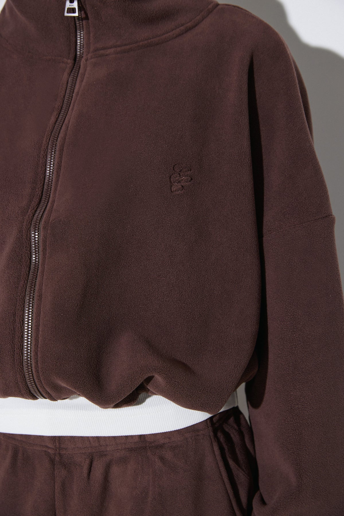 Detailaufnahme der dunkelbraunen Fleece-Jacke mit Reißverschluss, Stehkragen und einem dezenten Estro-Logo auf der Brust