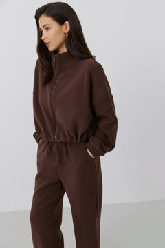 Schräge Seitenansicht des Models in der dunkelbraunen Fleece-Hose und dem passenden Oberteil mit Stehkragen