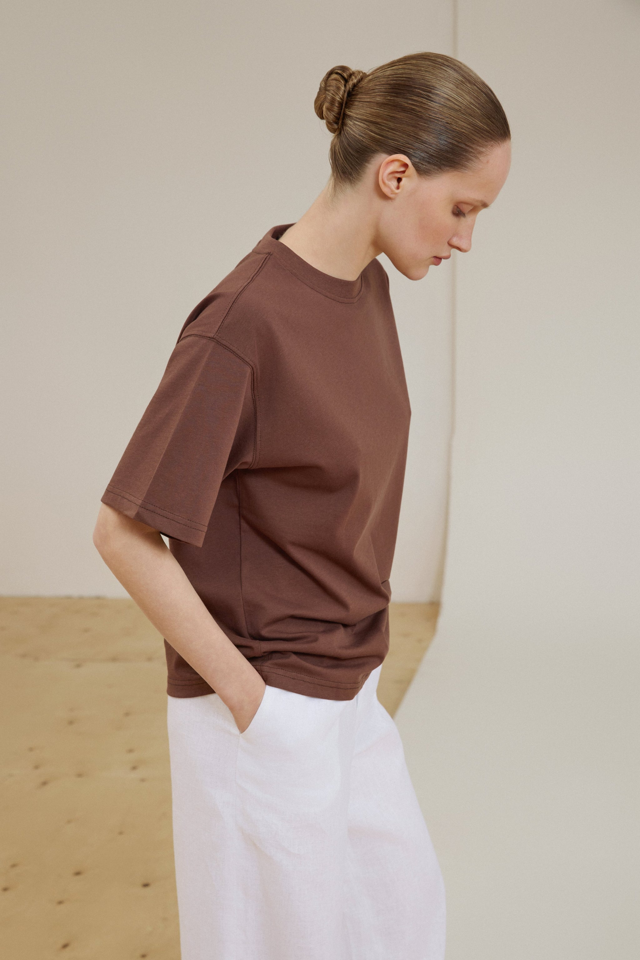 Seitenprofil des Models in braunem Oversize-T-Shirt und weißer Hose