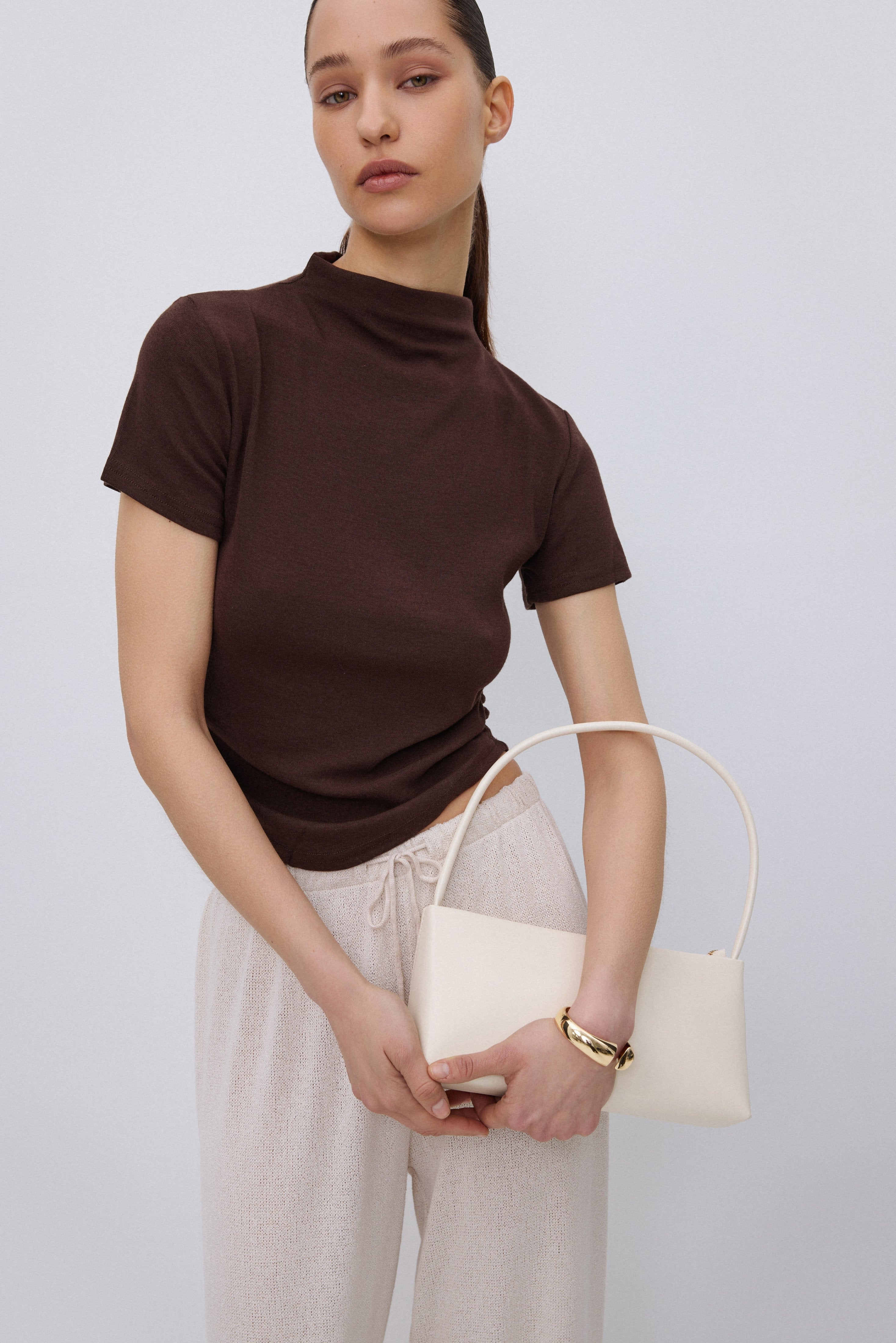 Das Model trägt das körpernahe dunkelbraune T-Shirt kombiniert mit einer hellen weiten Hose.