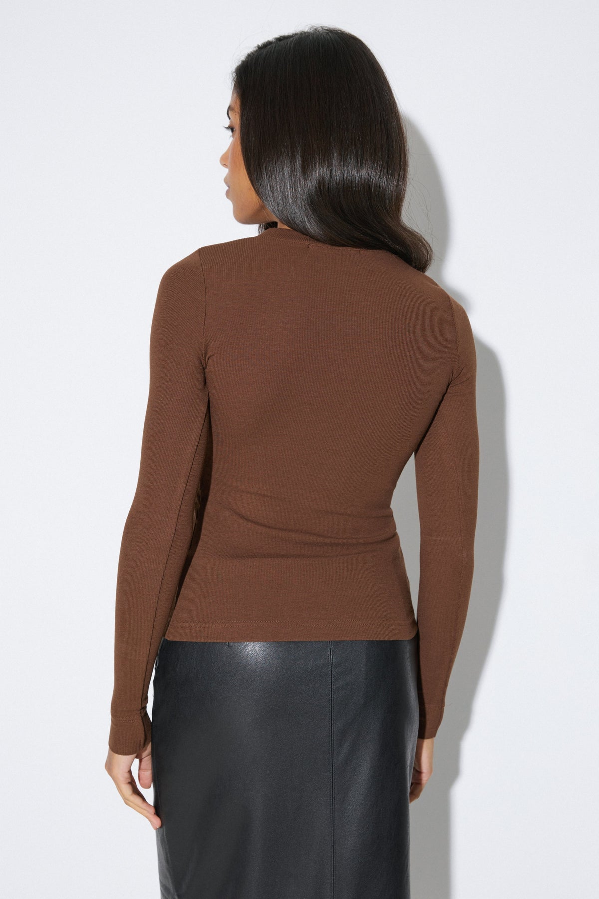 Studio-Aufnahme Rückseite: Rückenansicht der Frau im dunkelbraunen gerippten Damen-Longsleeve im passgenauen Slim Fit
