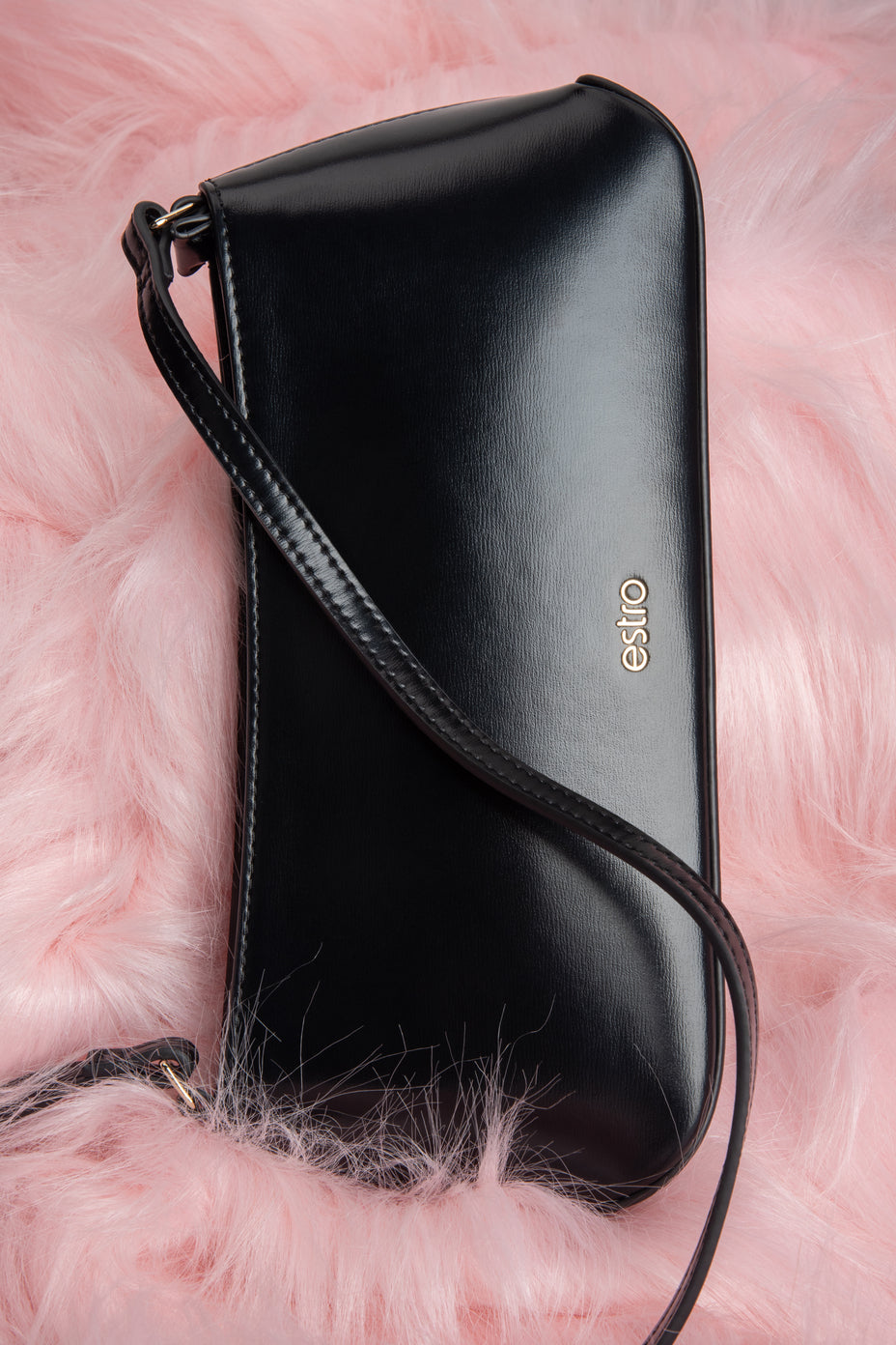 Künstlerische Draufsicht auf die schwarze Ledertasche, präsentiert auf einem flauschigen rosa Hintergrund 