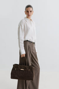 Kampagnenbild eines Models in weißer Bluse und weiter Stoffhose, das die dunkelbraune Velours-Handtasche trägt