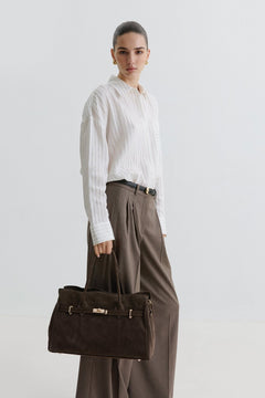 Kampagnenbild eines Models in weißer Bluse und weiter Stoffhose, das die dunkelbraune Velours-Handtasche trägt