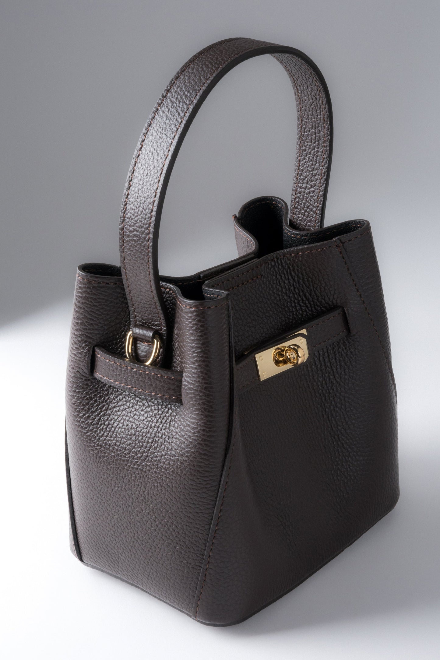 Frontale Schrägansicht der kompakten dunkelbraunen Leder-Henkeltasche mit goldenem Drehverschluss und genarbter Struktur 