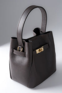Frontale Schrägansicht der kompakten dunkelbraunen Leder-Henkeltasche mit goldenem Drehverschluss und genarbter Struktur 