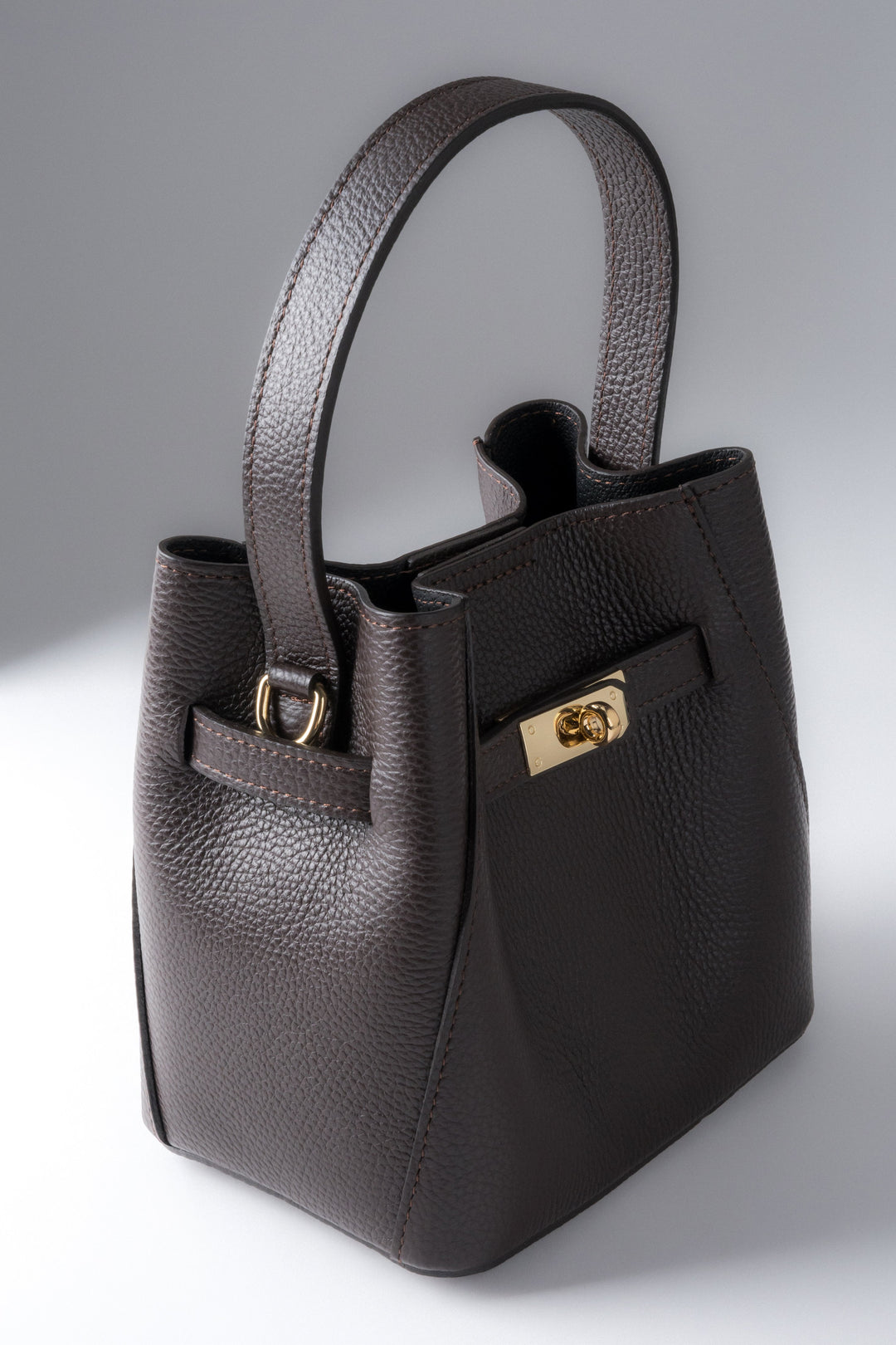 Frontale Schrägansicht der kompakten dunkelbraunen Leder-Henkeltasche mit goldenem Drehverschluss und genarbter Struktur 