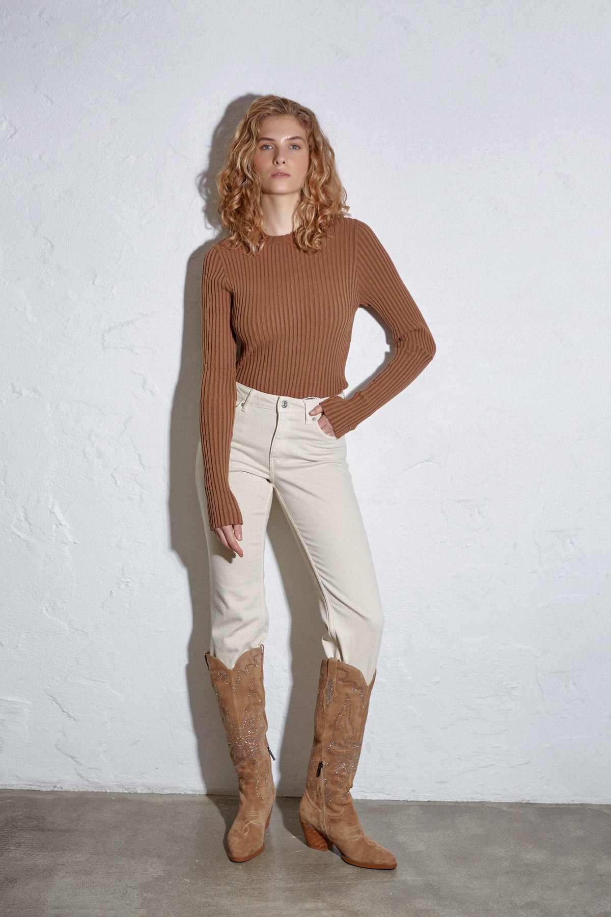 Model trägt die hellbeigen Velours-Cowboystiefel zu einer hellen Jeans und braunem Oberteil