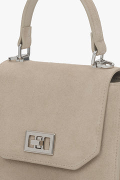 Detailaufnahme der Lederstruktur und des Schnallenverschlusses der hellbeigen Tasche.