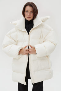 Model präsentiert die offene hellbeige Oversize-Pufferjacke mit hohem Kragen und schwarzem Rollkragenpullover
