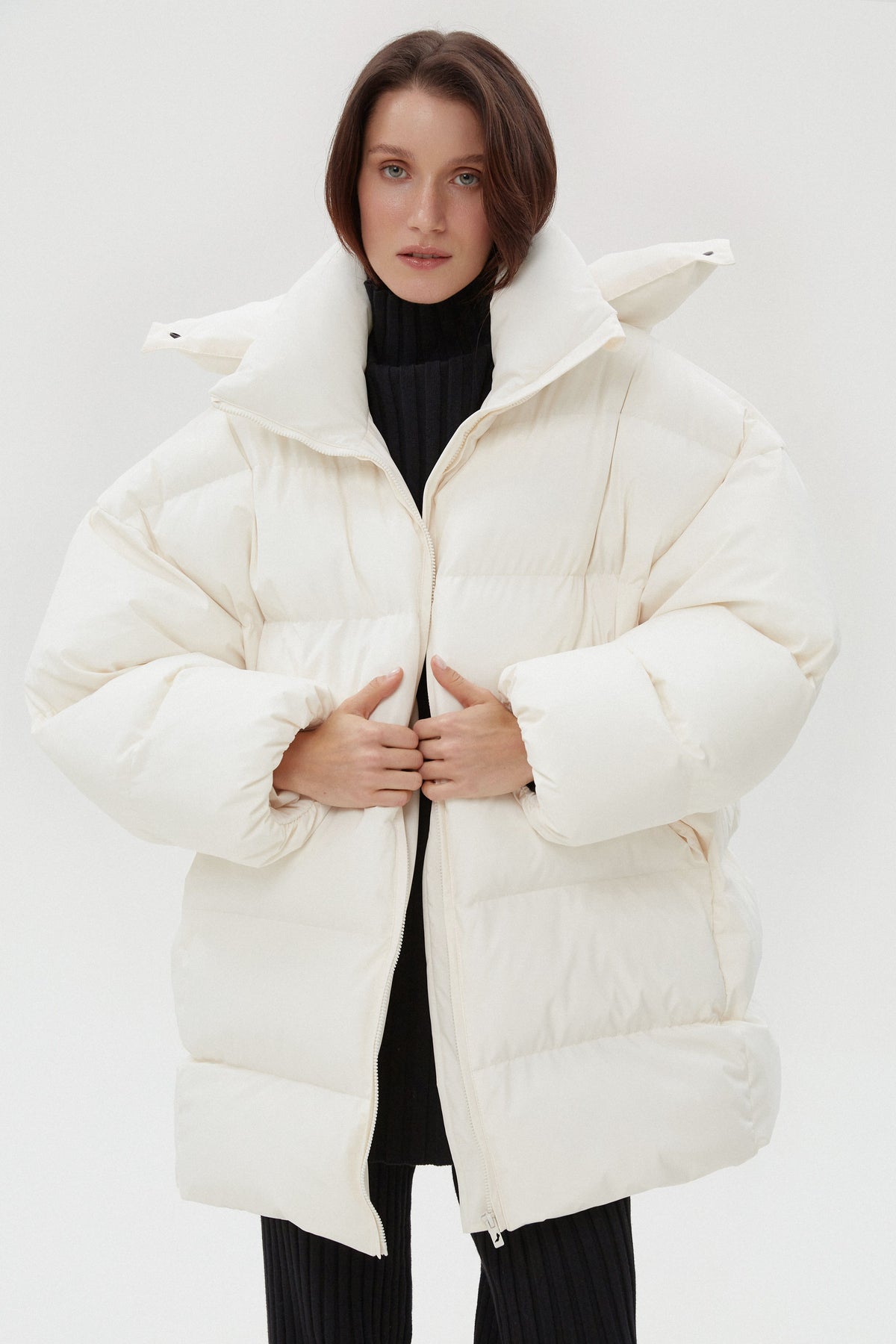 Model präsentiert die offene hellbeige Oversize-Pufferjacke mit hohem Kragen und schwarzem Rollkragenpullover