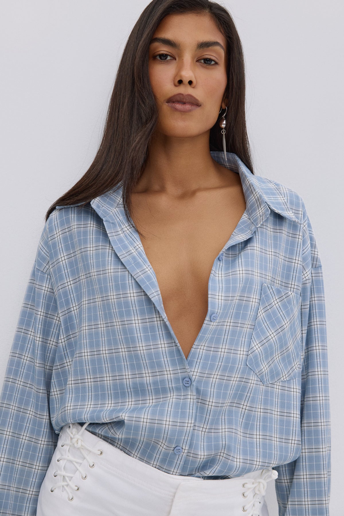 Nahaufnahme des Models in der leicht geöffneten, hellblau-weiß karierten Oversize-Hemdbluse