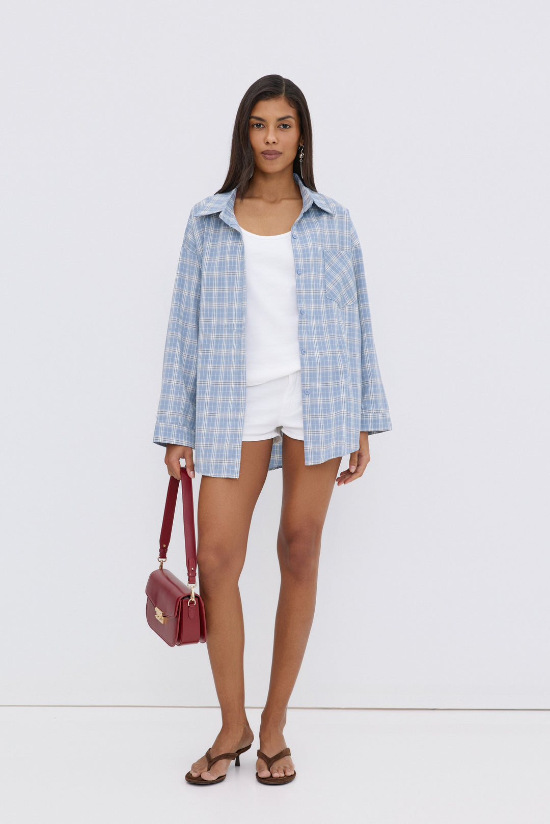 Model trägt die hellblaue Karo-Hemdbluse offen über einem weißen Top und weißen Shorts, mit einer roten Handtasche