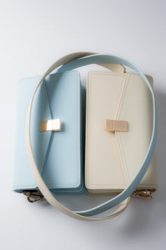 Hellblaue und milchbeige Damenhandtaschen aus Leder mit langem Schulterriemen.