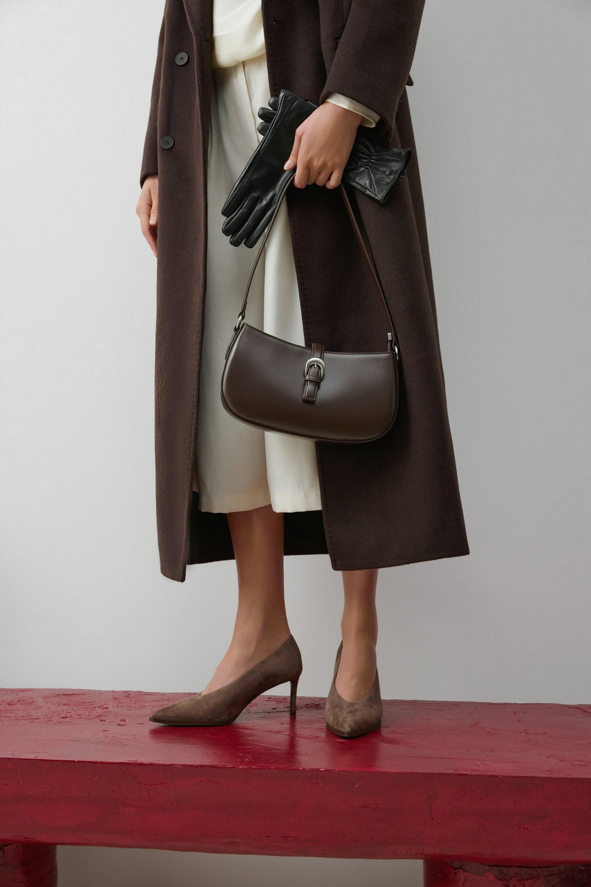 Model im braunen Mantel hält die kleine dunkelbraune Estro Tasche in der Hand