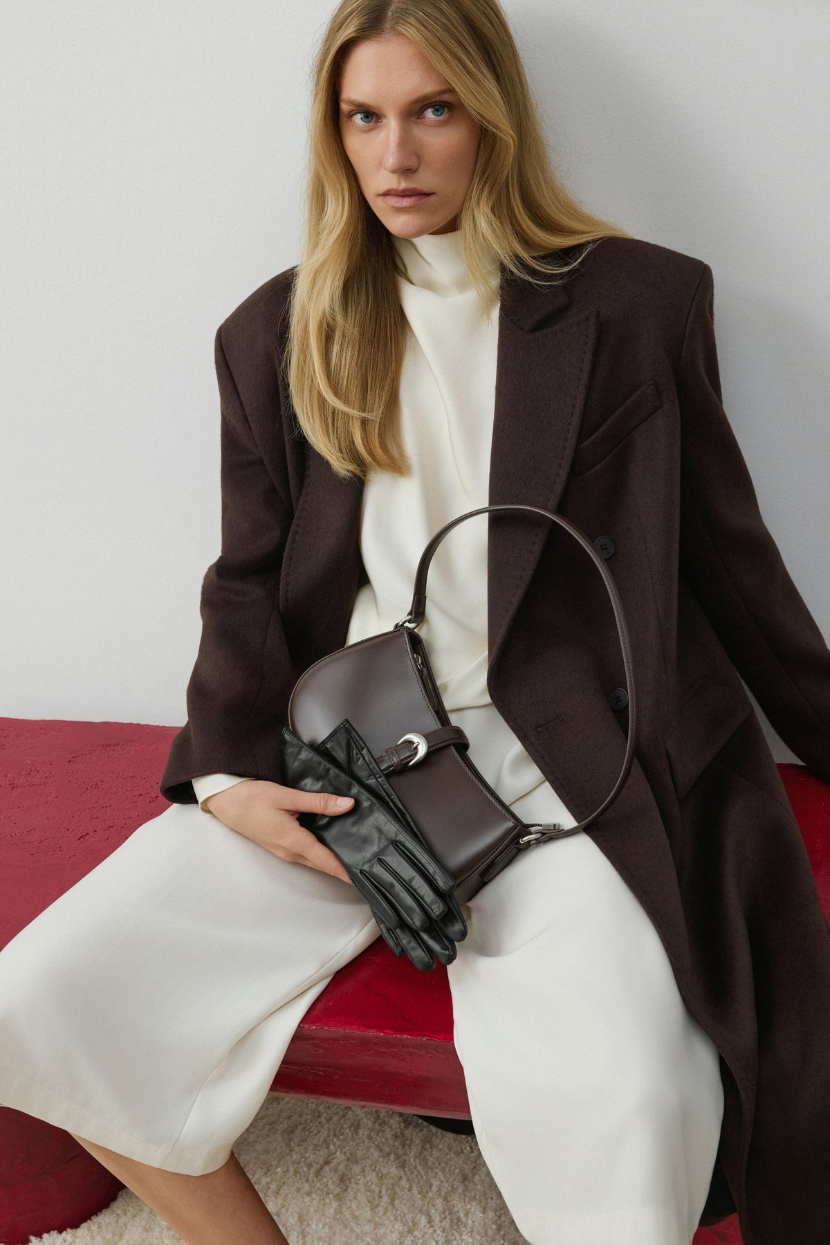 Model in hellem Outfit sitzt und trägt die dunkelbraune Tasche lässig als Crossbody-Bag