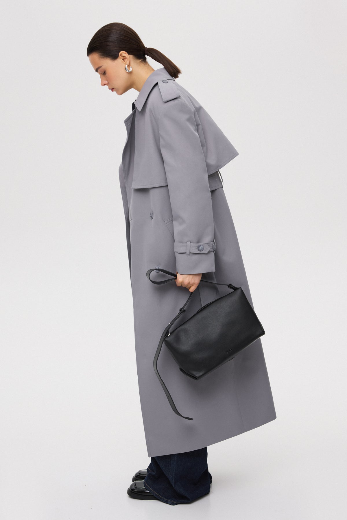 Model präsentiert die schwarze Damen-Umhängetasche zum grauen Trenchcoat
