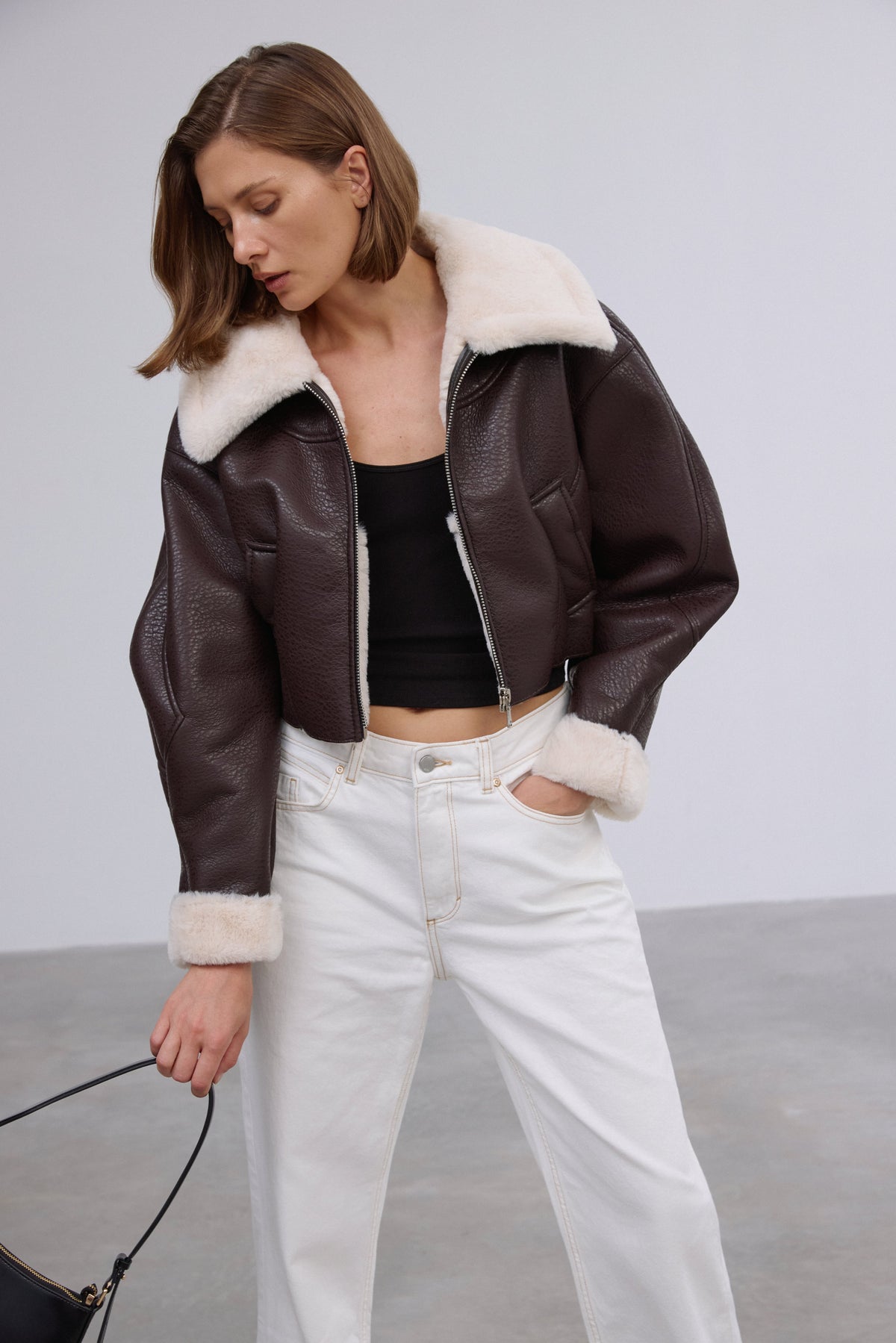 Halblange Frontalansicht des Models in der offenen dunkelbraunen Shearling-Jacke mit Reißverschluss
