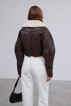 Rückansicht des Models, die den cropped Schnitt und den breiten hellen Fellkragen der dunkelbraunen Jacke zeigt