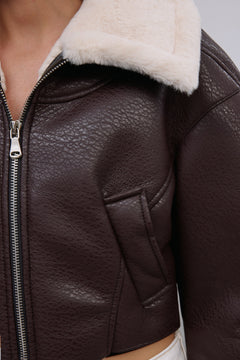 Detailaufnahme der Narbenleder-Textur, des Metall-Reißverschlusses und des hellen Kunstfells der dunkelbraunen Jacke