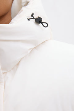 Detailaufnahme des hohen Stehkragens und der Kapuze der milchbeigen Pufferjacke mit Kordelzug 