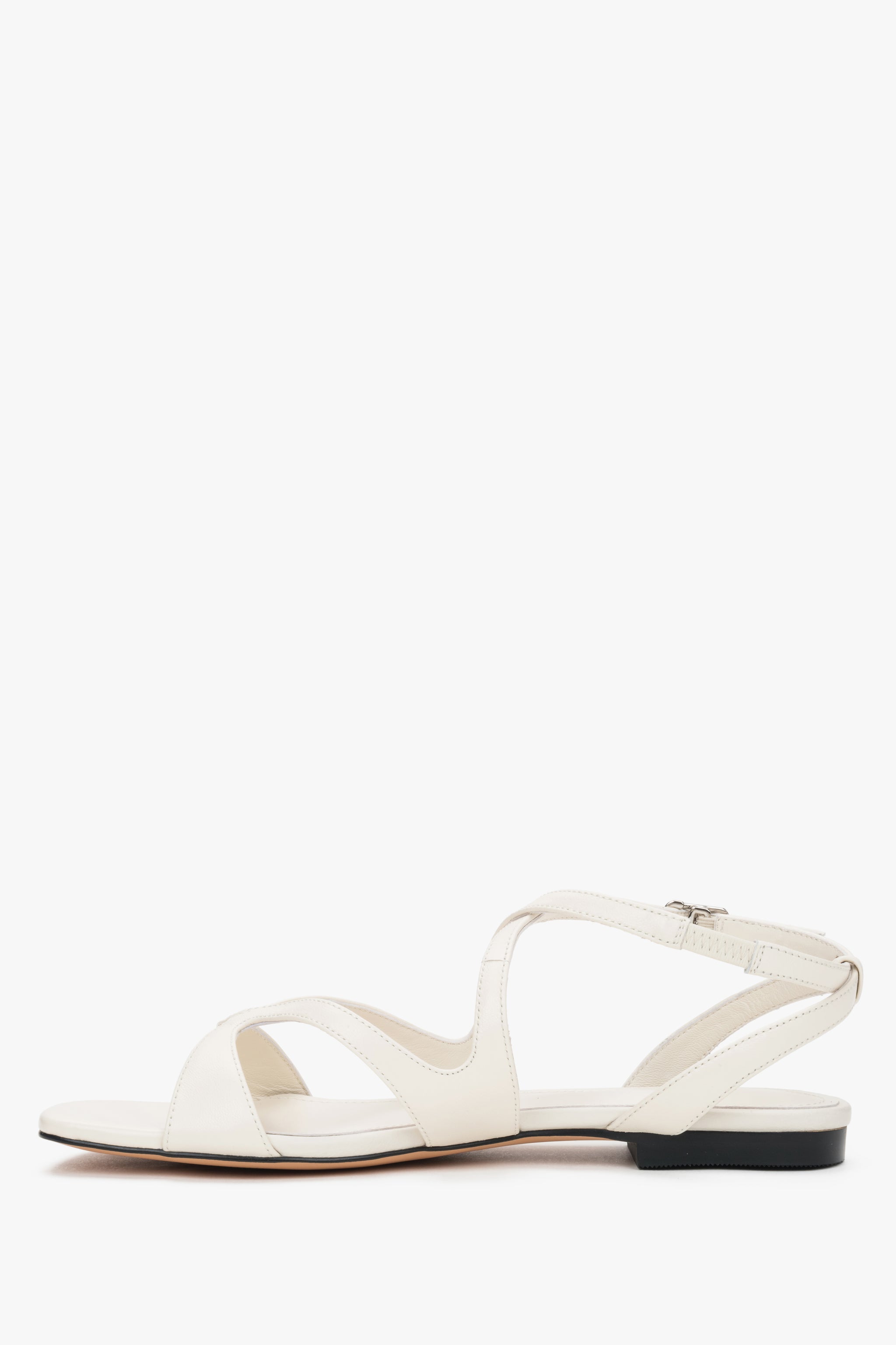 Linkes Seitenprofil der cremefarbenen Sandalen mit gekreuzten Riemen.