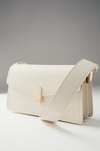 Frontalansicht der milchbeigen Damen-Schultertasche aus Leder mit goldenen Details.
