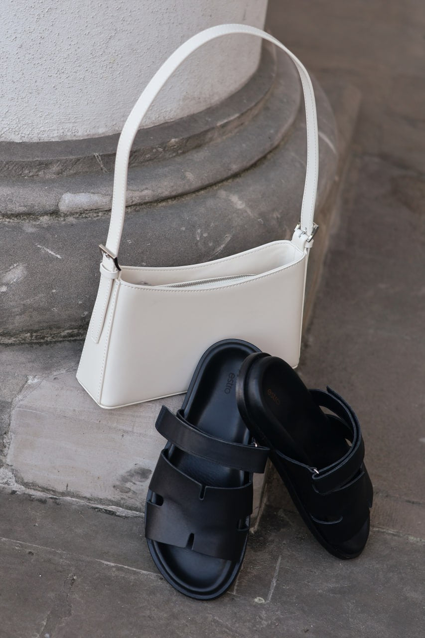 Milchbeige Damen-Schultertasche aus Echtleder neben schwarzen Pantoletten