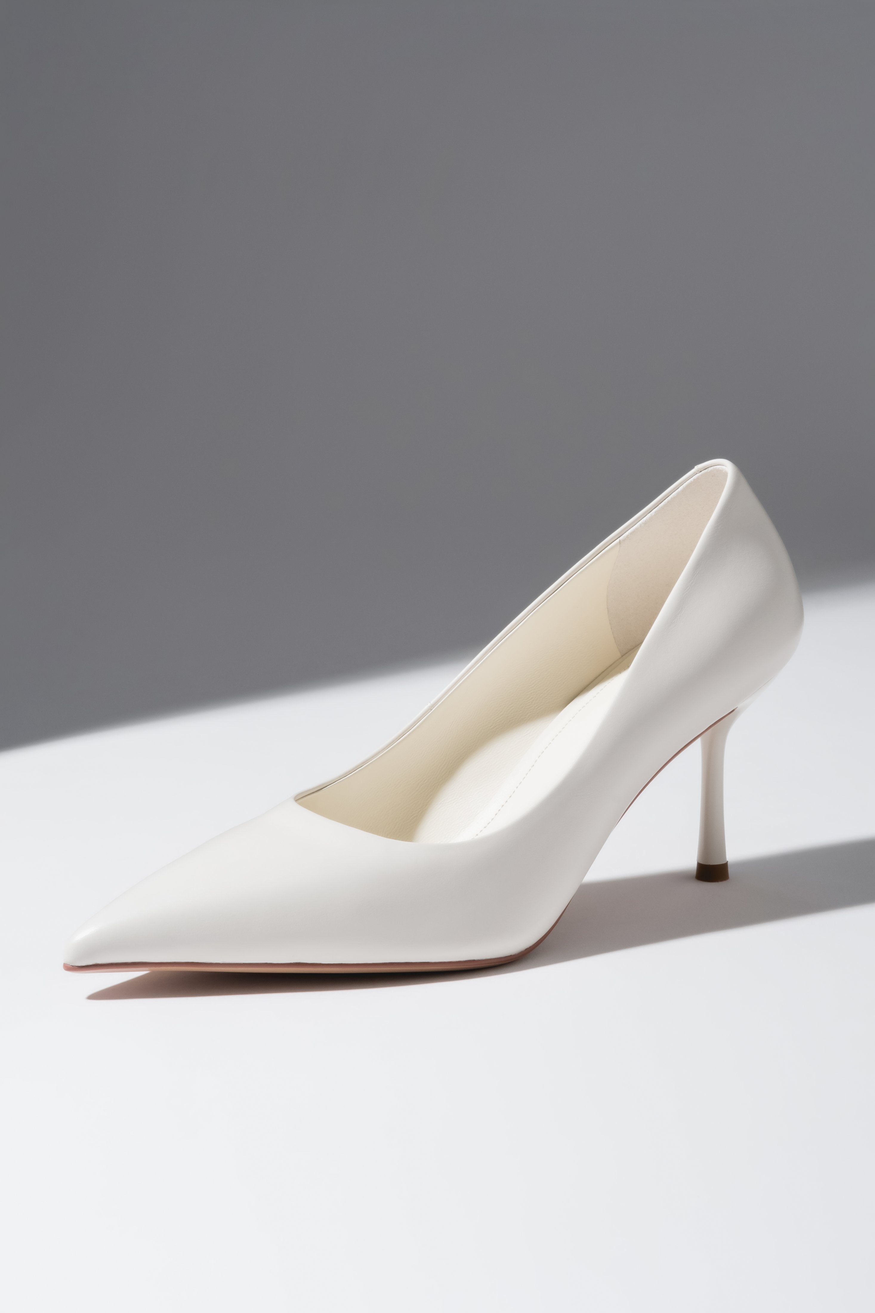 Kreative Schrägansicht der milchbeigen Damen-Stilettos aus Echtleder, übereinander platziert mit Fokus auf die spitze Kappe und den Absatz 