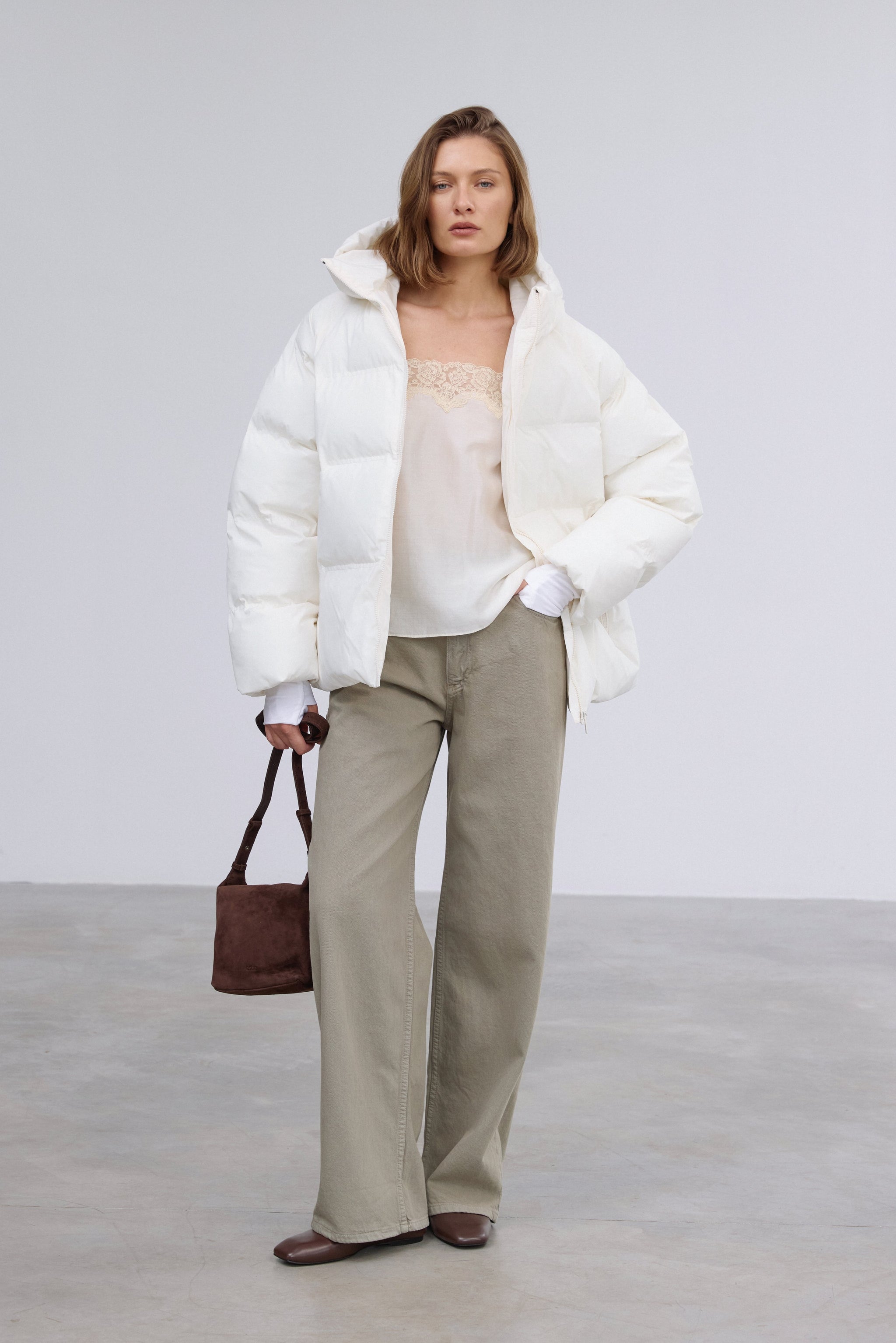 Frontalansicht der milchbeigen Damen-Winterjacke im Loose-Fit, halboffen getragen über einem lässigen Outfit mit dunkler Handtasche