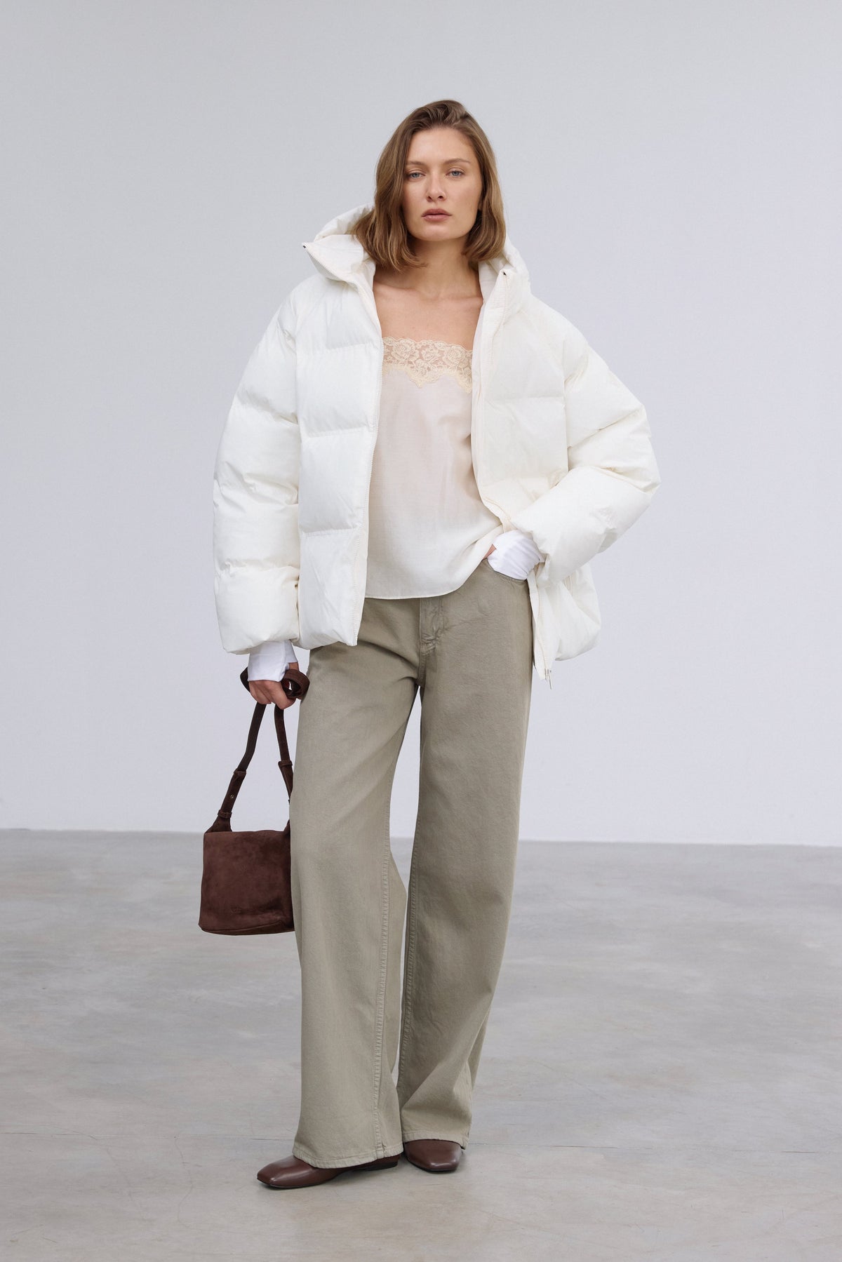 Frontalansicht der milchbeigen Damen-Winterjacke im Loose-Fit, halboffen getragen über einem lässigen Outfit mit dunkler Handtasche