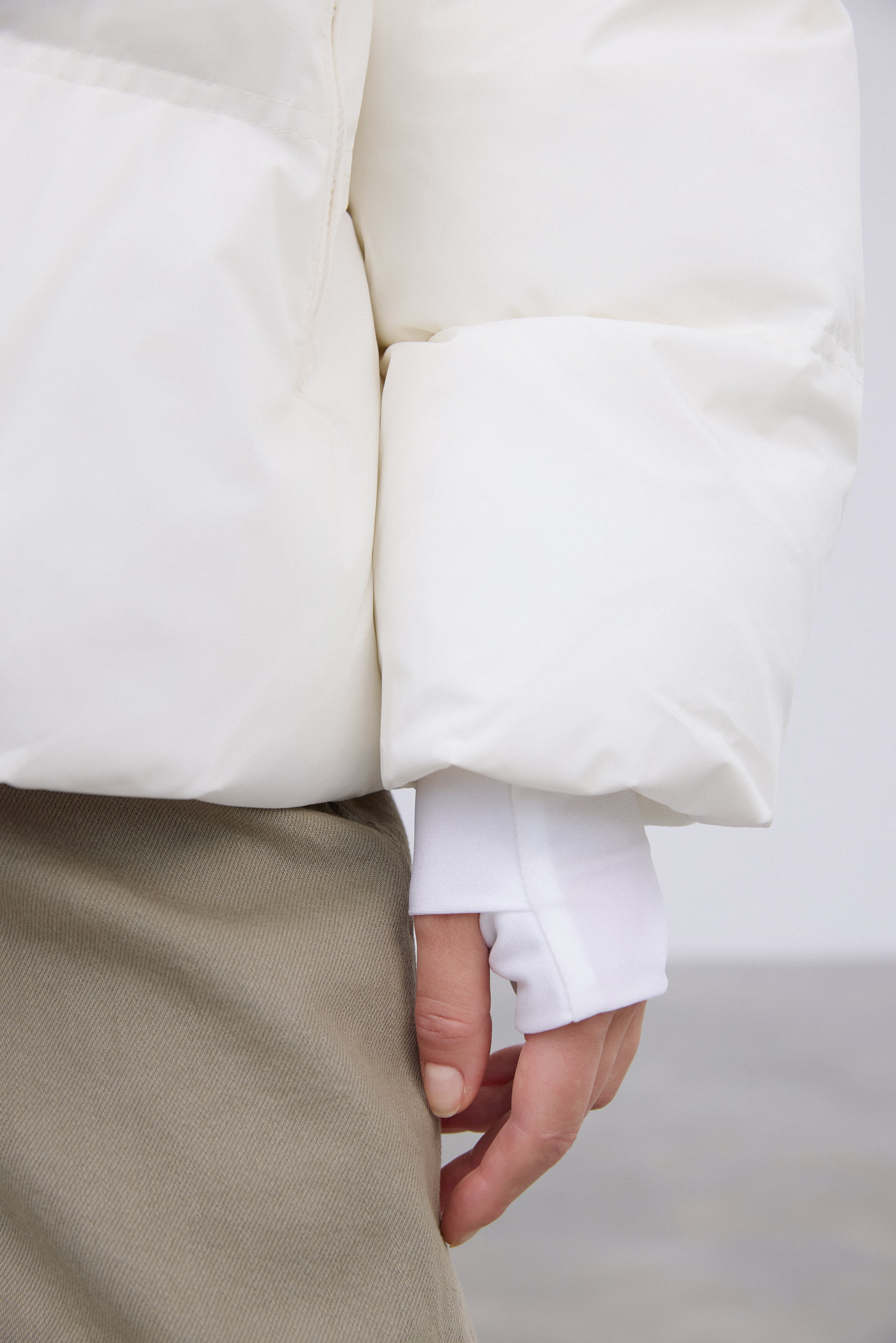 Detailaufnahme des Ärmels der milchbeigen Pufferjacke mit Fokus auf das verlängerte, enganliegende Bündchen 