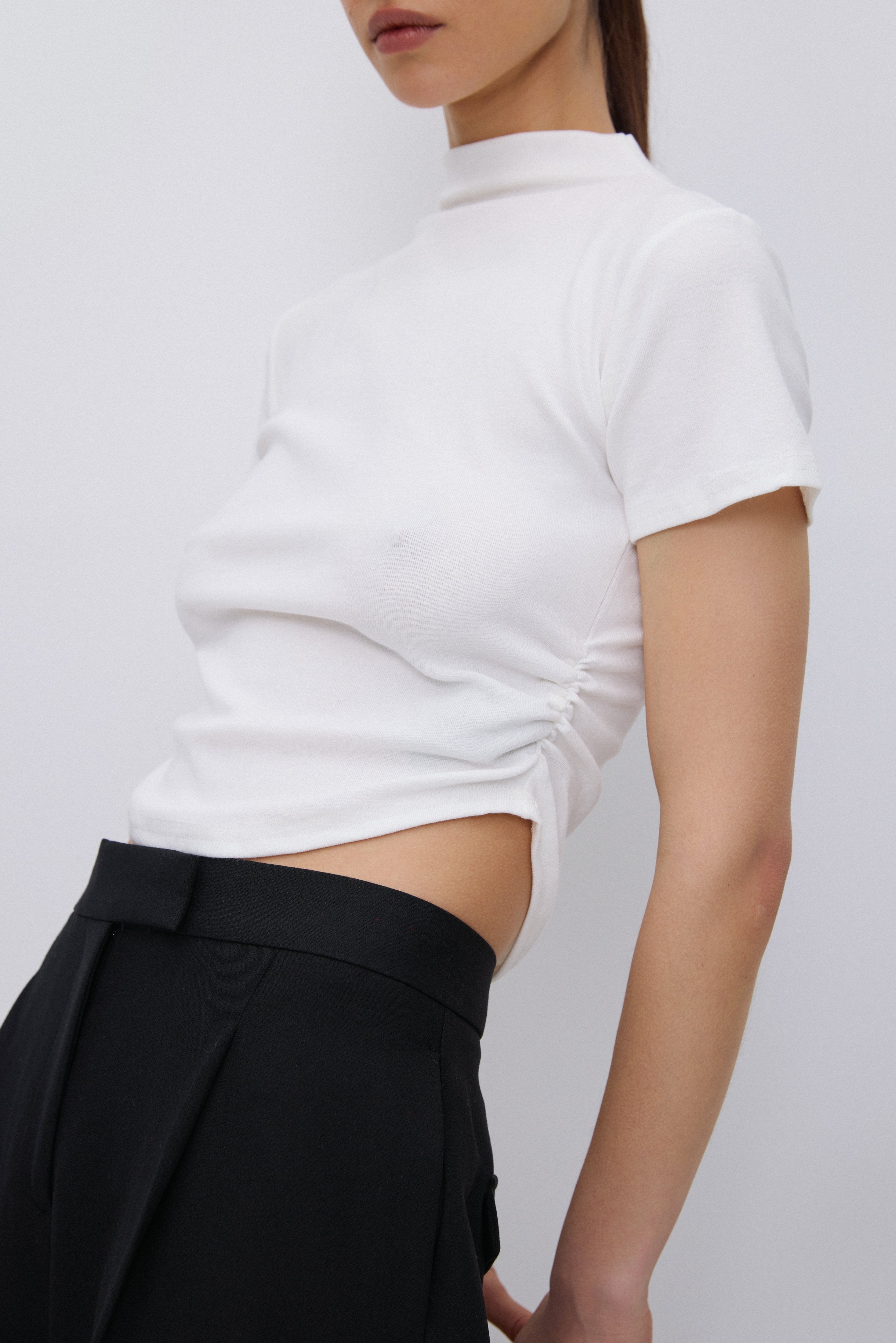Seitenansicht des T-Shirts, die die asymmetrische Raffung an der Taille deutlich zeigt.