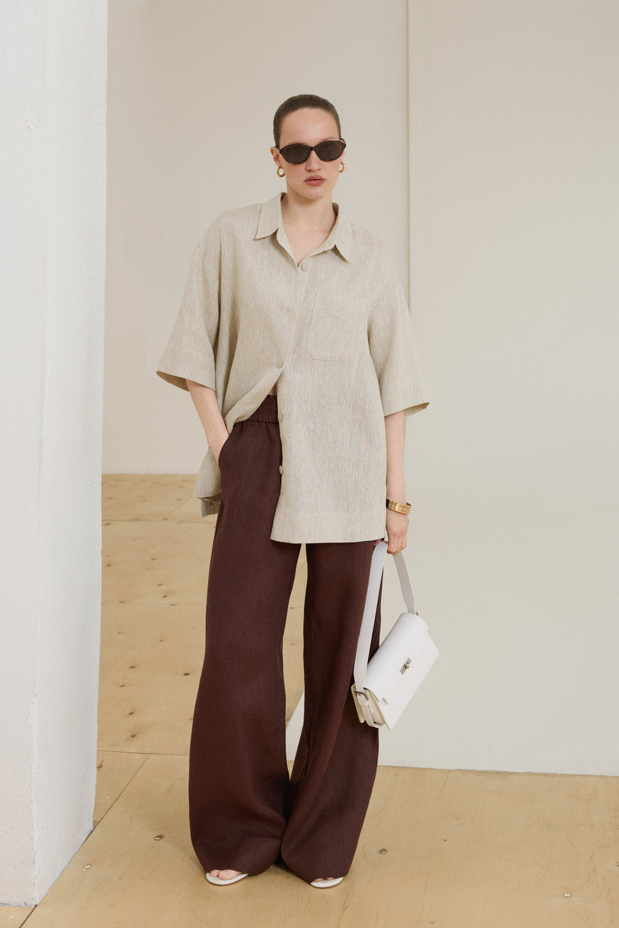Model steht in einem eleganten, hellen Sommeroutfit und präsentiert die milchweiße Schultertasche