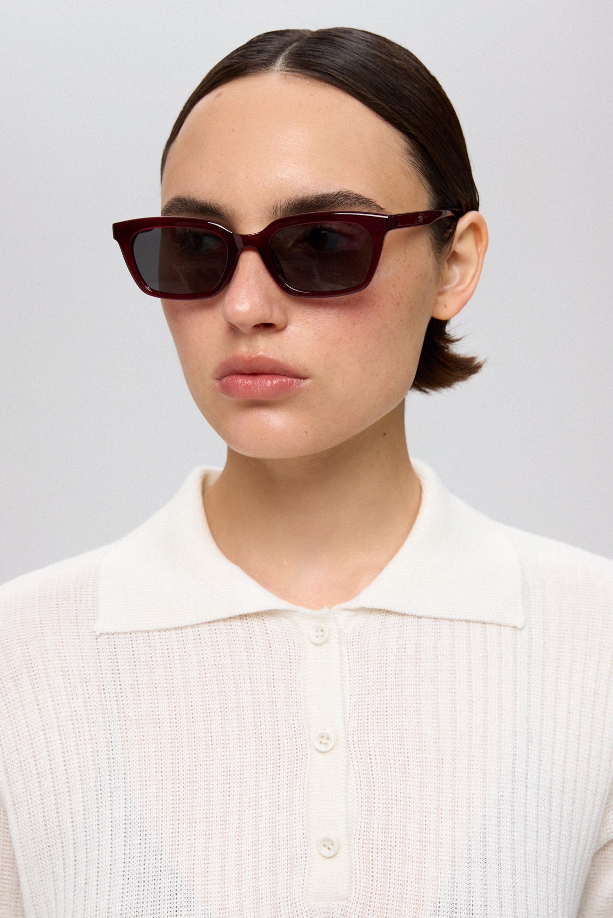 Model trägt die bordeauxrote, rechteckige Damen-Sonnenbrille zu einem hellen Poloshirt 