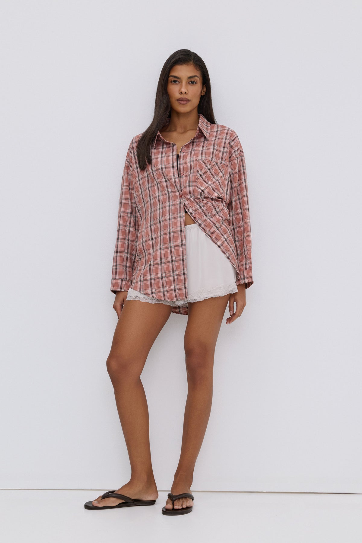 Frontansicht des Models, das die rosa Karo-Bluse offen über einem schwarzen Top und weißen Shorts trägt