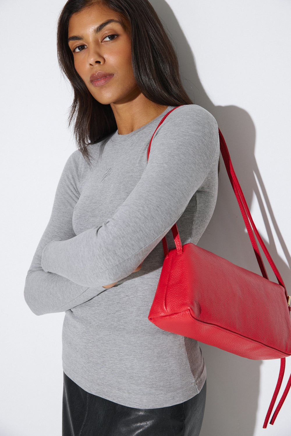 Stilvolle Lifestyle-Aufnahme eines Models im schlichten grauen Pullover, das die leuchtend rote Schultertasche aus genarbter italienischer Premium-Leder präsentiert.