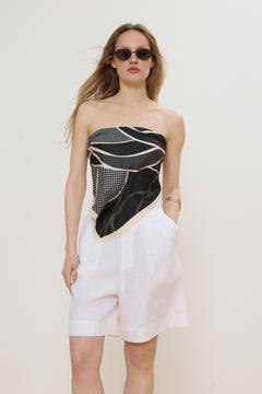 Model trägt das schwarz-beigefarbene Halstuch als stilvolles Bandeau-Oberteil zu weißen Shorts