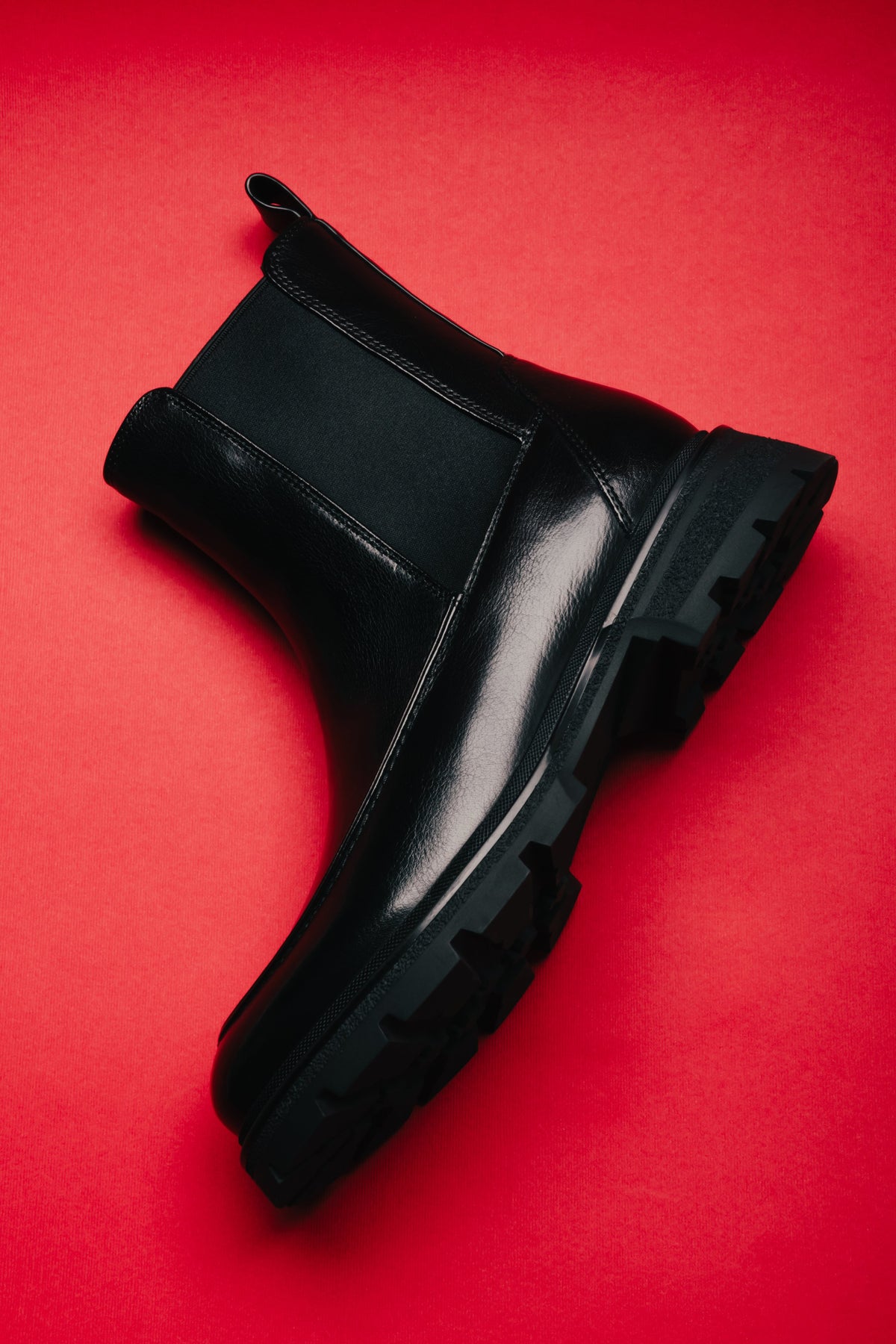 Flaches Seitenprofil des schwarzen Chelsea-Boots auf rotem Hintergrund