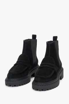 Studioaufnahme von zwei knöchelhohen, schwarzen Damen-Chelsea-Boots aus echtem Veloursleder auf hellem, neutralem Hintergrund.