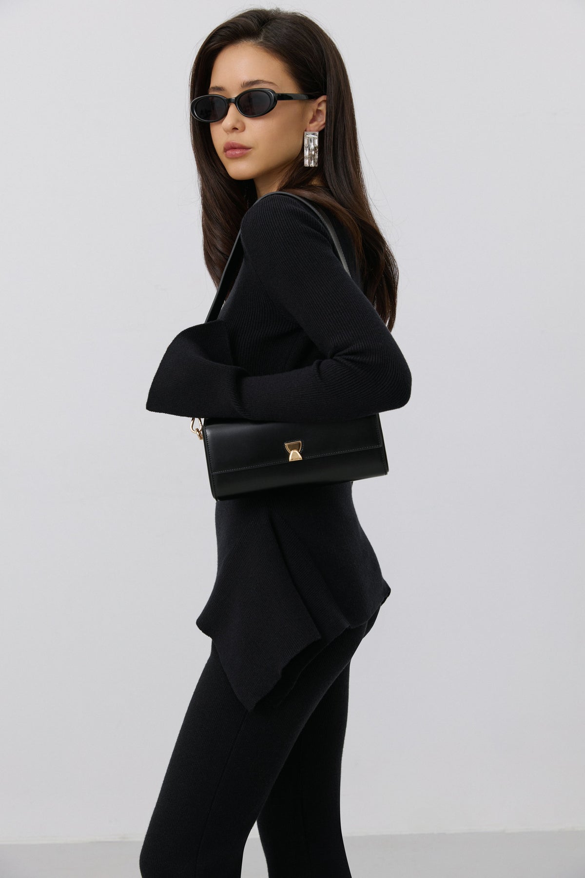Model im komplett schwarzen Outfit mit Sonnenbrille trägt die schwarze Leder-Clutch elegant unter dem Arm