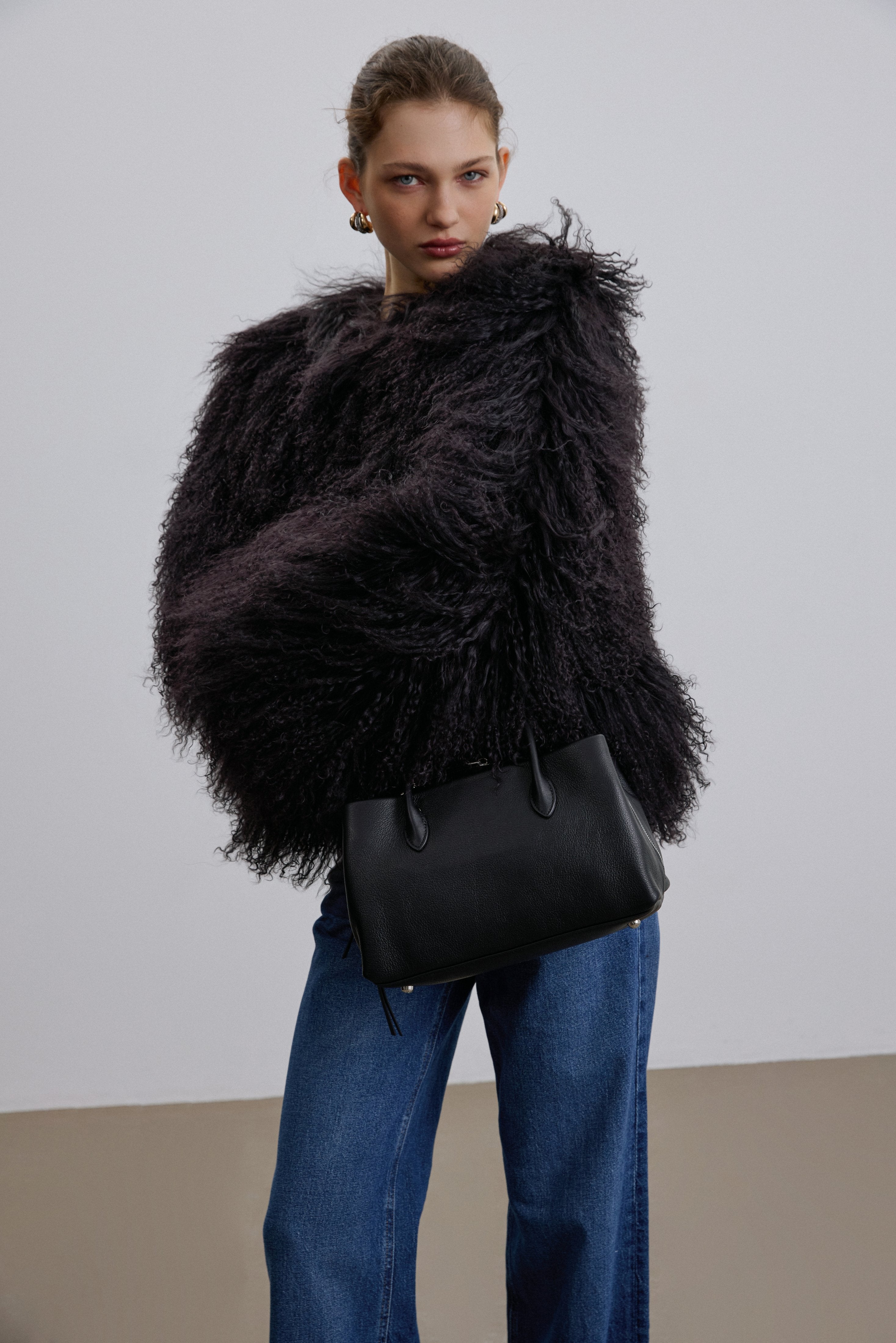 Model trägt die schwarze Handtasche zu einem dunklen, pelzigen Outfit für einen modernen, stilvollen Auftritt