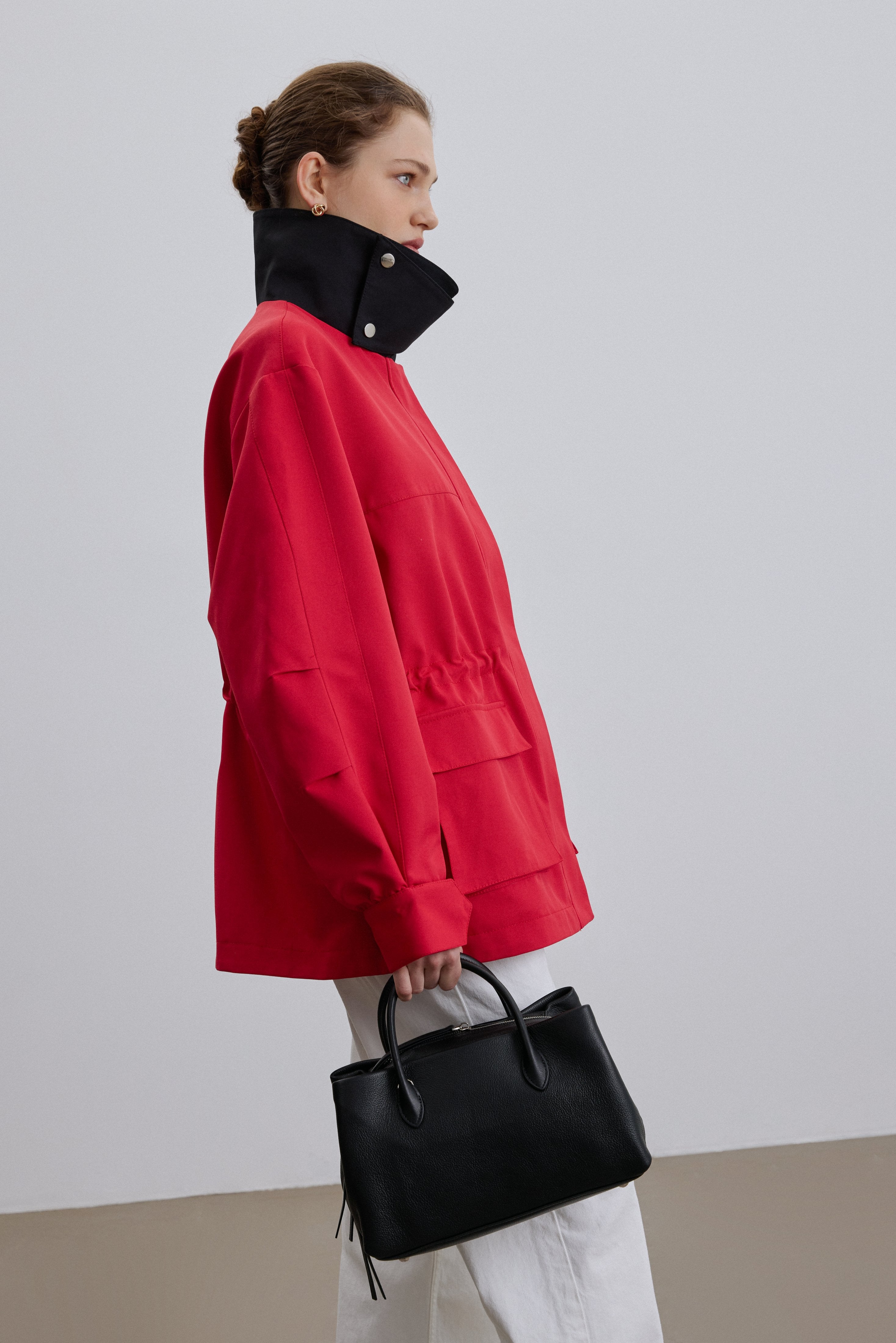 Model in roter Jacke präsentiert die schwarze Handtasche als stilvolles Accessoire in einer urbanen Umgebung 