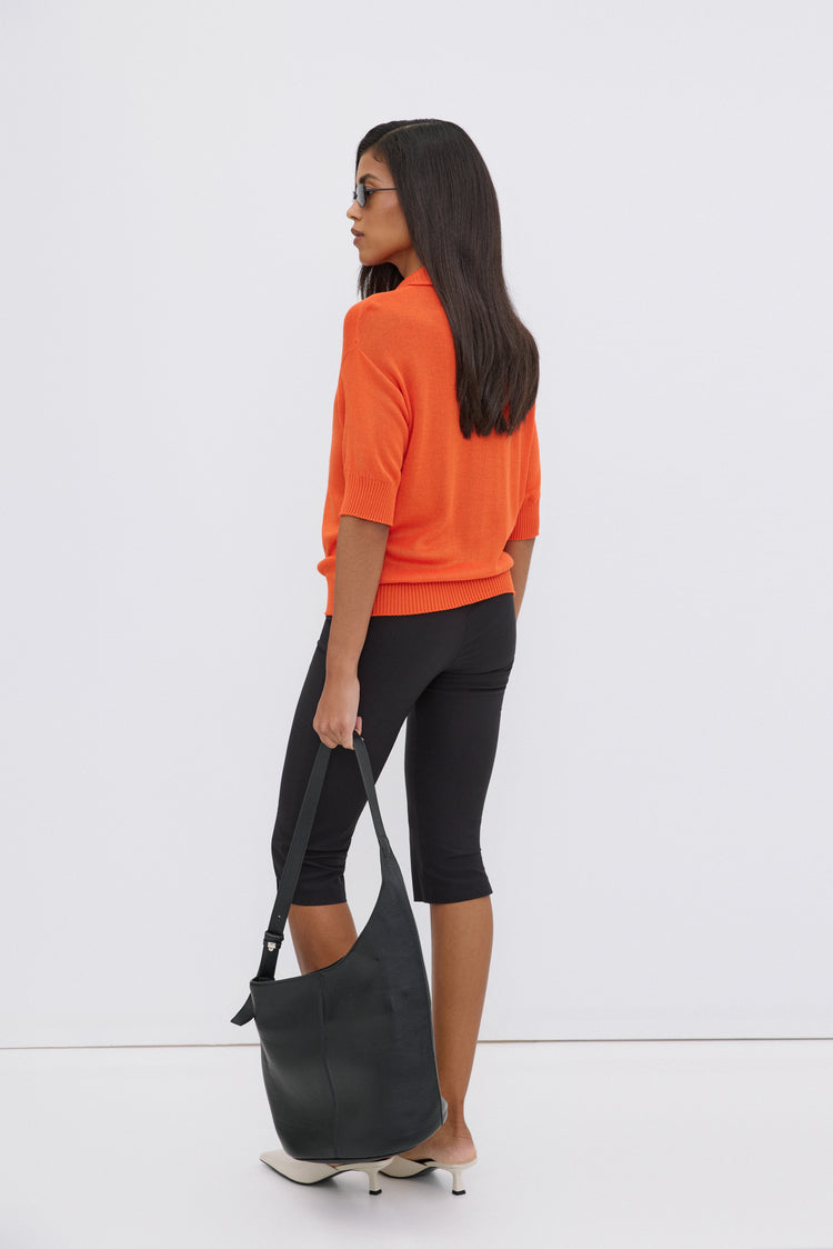Model in Seitenansicht mit orangefarbenem Oberteil, trägt die schwarze Echtleder-Hobo-Tasche lässig in der Hand