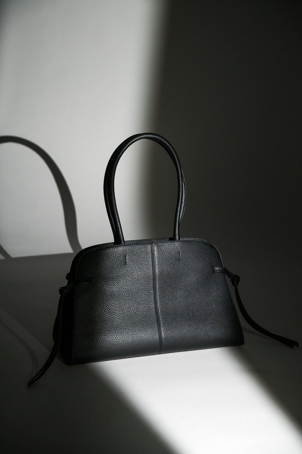 Künstlerische Studioaufnahme der schwarzen Leder-Koffertasche mit seitlichen Bindebändern im dramatischen Licht