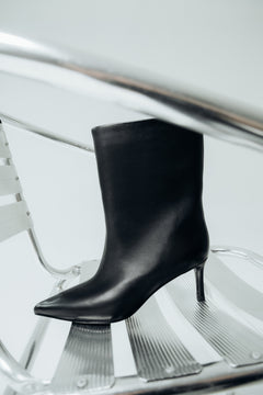 Diagonale Frontalansicht der schwarzen Stiefelette mit verlängerter spitzer Zehenpartie auf einem Stuhl präsentiert