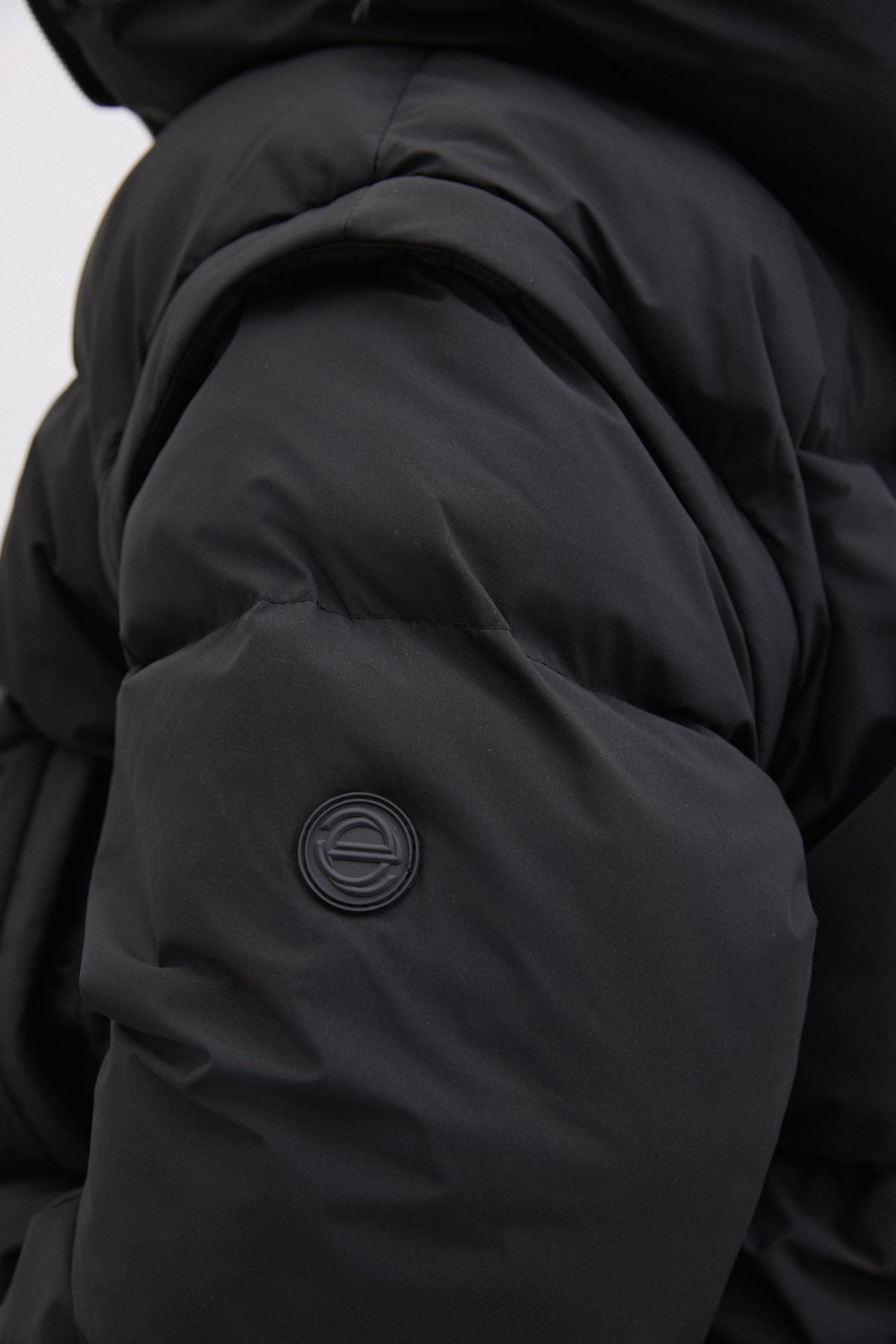Detailaufnahme des Ärmels der schwarzen Pufferjacke, die das matte Obermaterial und die Steppung hervorhebt