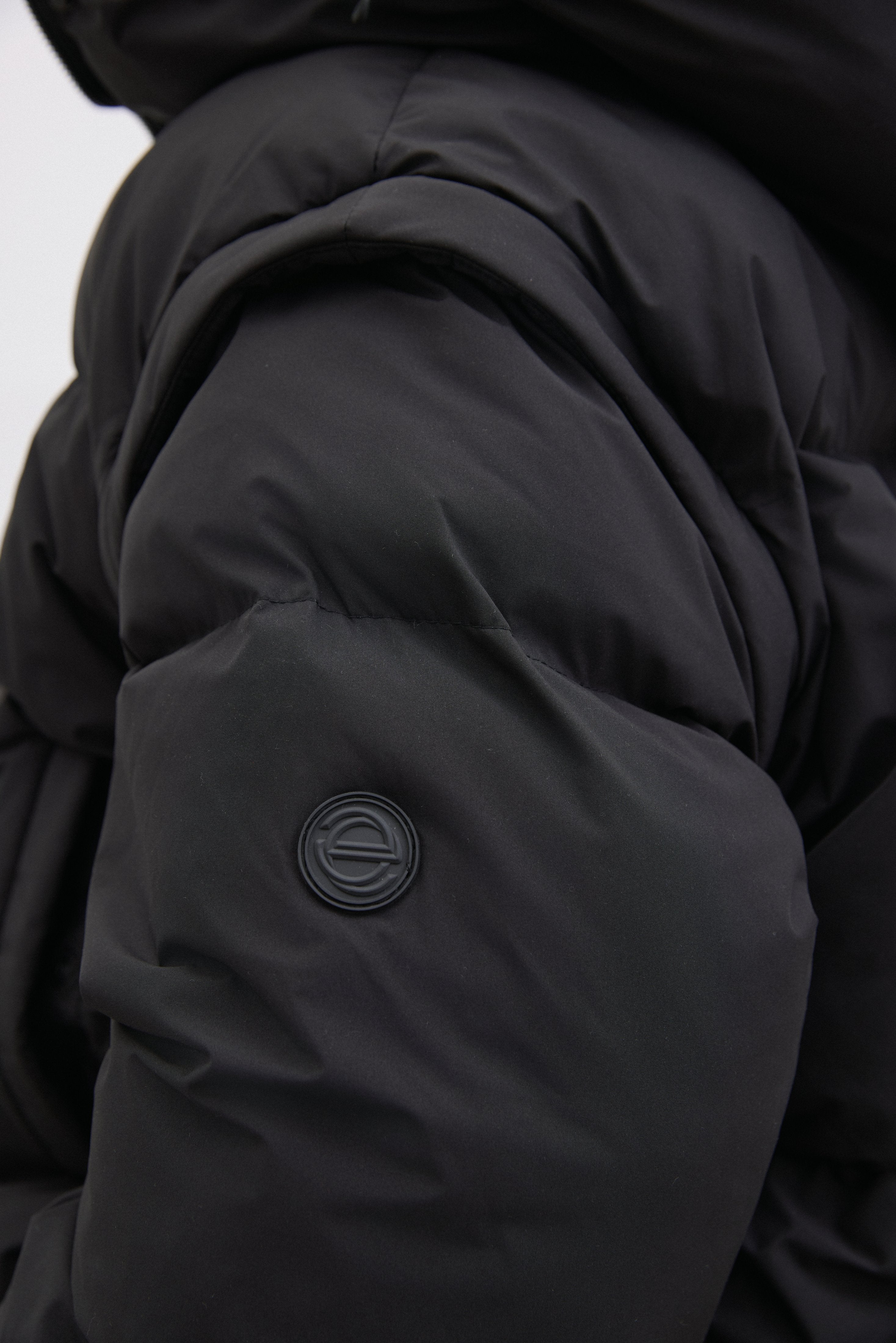 Detailaufnahme des Ärmels der schwarzen Pufferjacke, die das matte Obermaterial und die Steppung hervorhebt