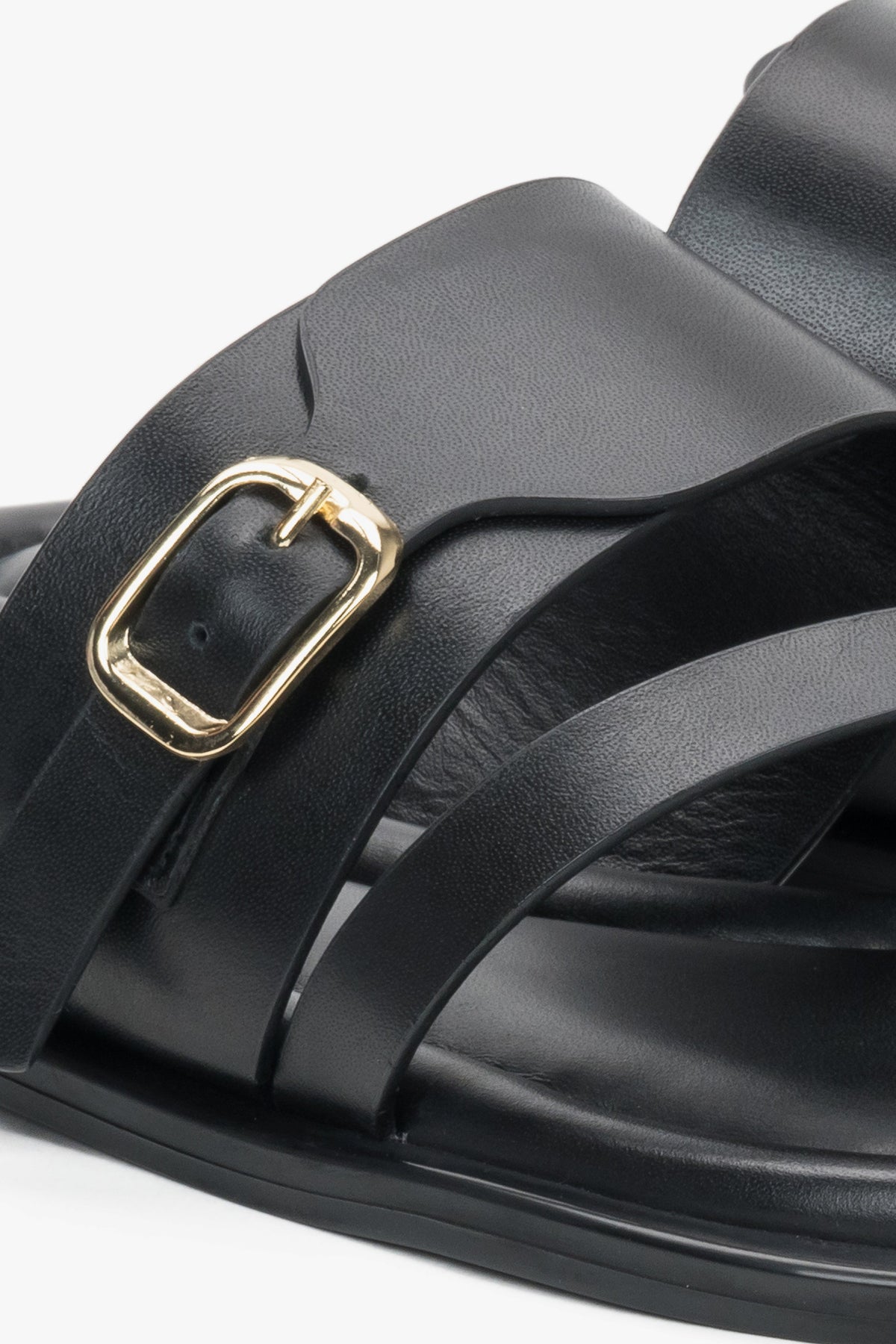 Detailaufnahme schwarzer Damen-Pantoletten mit goldfarbener Schnalle und Zehenschlaufe