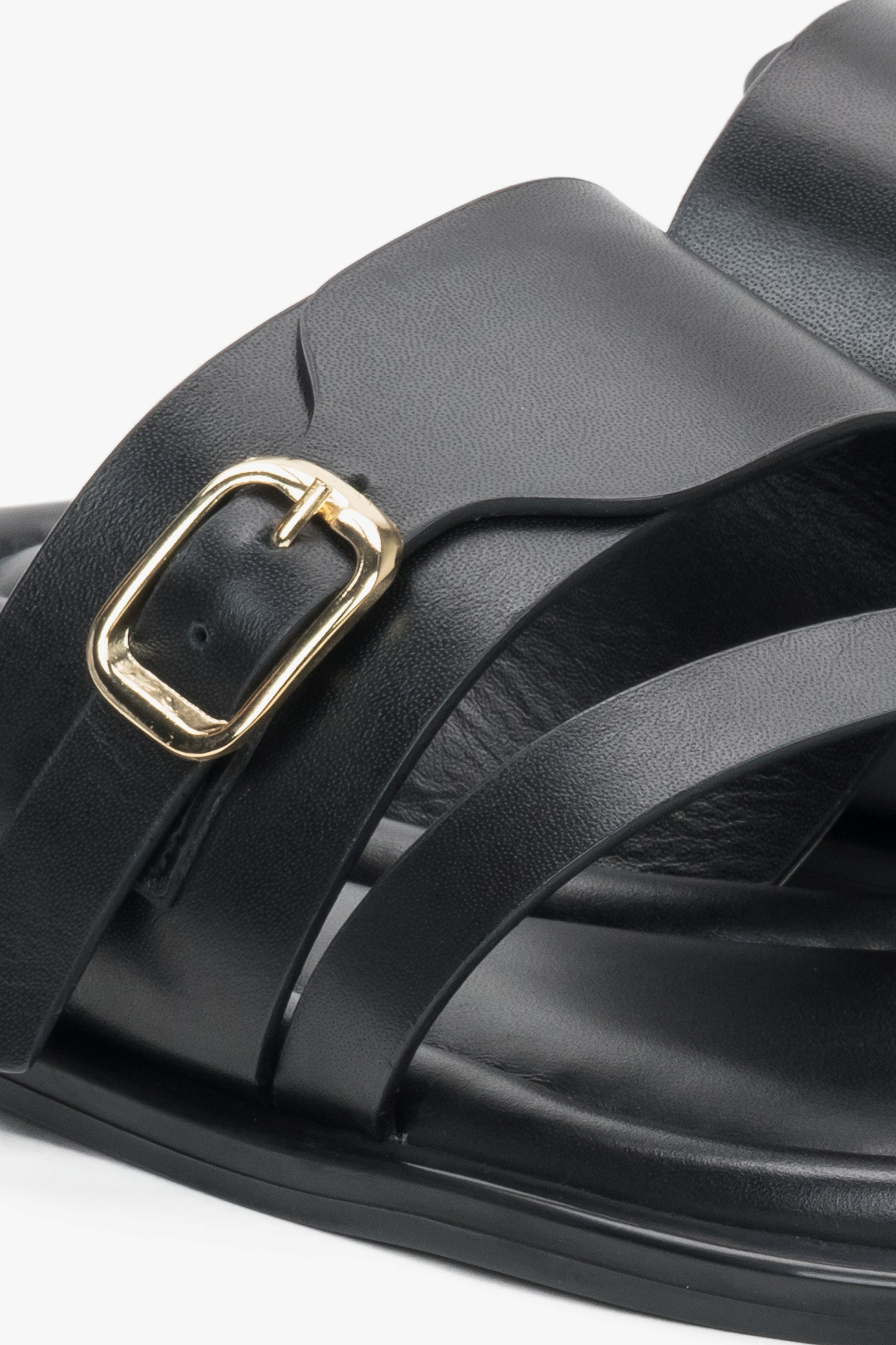 Detailaufnahme schwarzer Damen-Pantoletten mit goldfarbener Schnalle und Zehenschlaufe